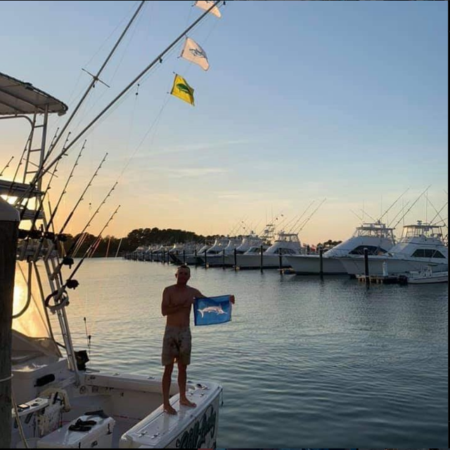 A man standing on a boat holding a fish flag