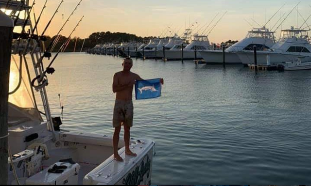 A man is standing on a boat holding a flag with a fish on it.