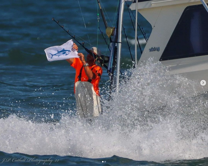A man on a boat holding a flag with a fish on it