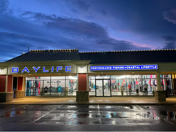 Baylife store exterior lit up at dusk, selling coastal lifestyle apparel.