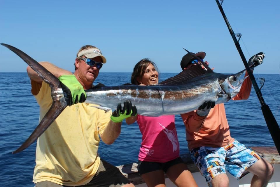 Two men and a woman holding a large sailfish on a boat