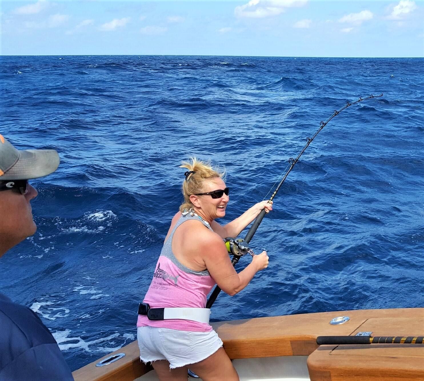 A woman in a pink tank top is fishing in the ocean