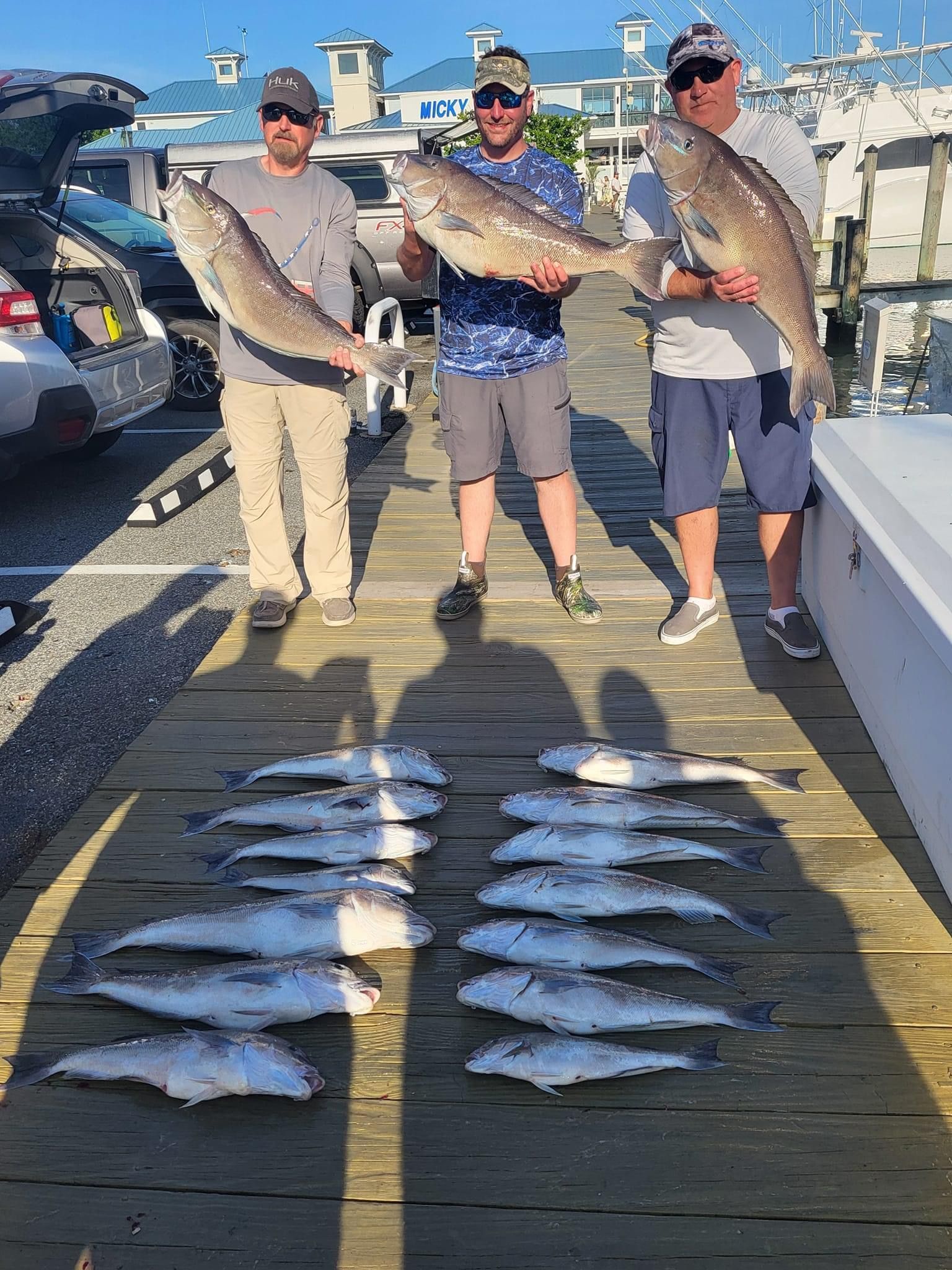 Three men are standing on a dock holding large fish