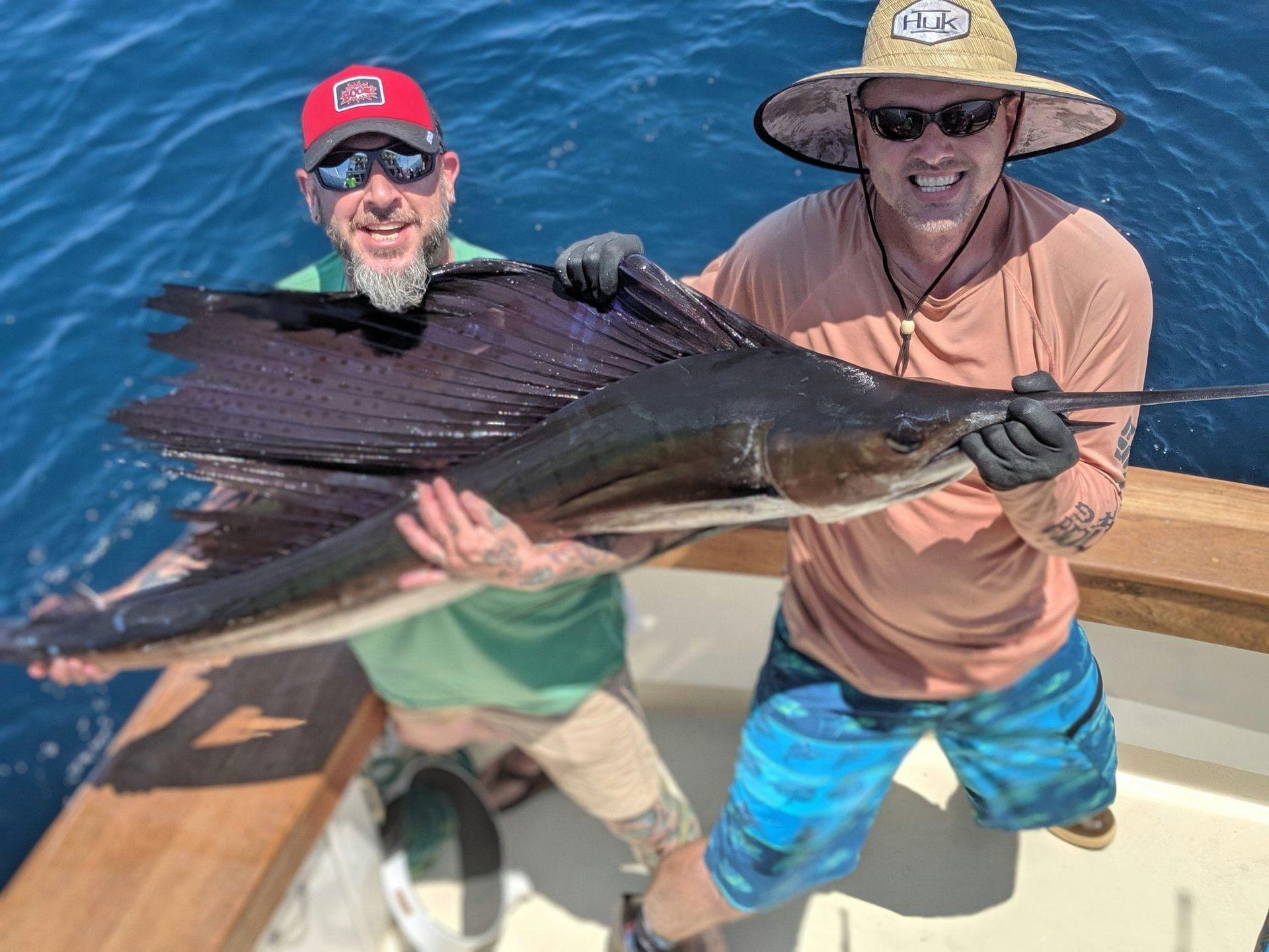 Two men on a boat holding a large sailfish