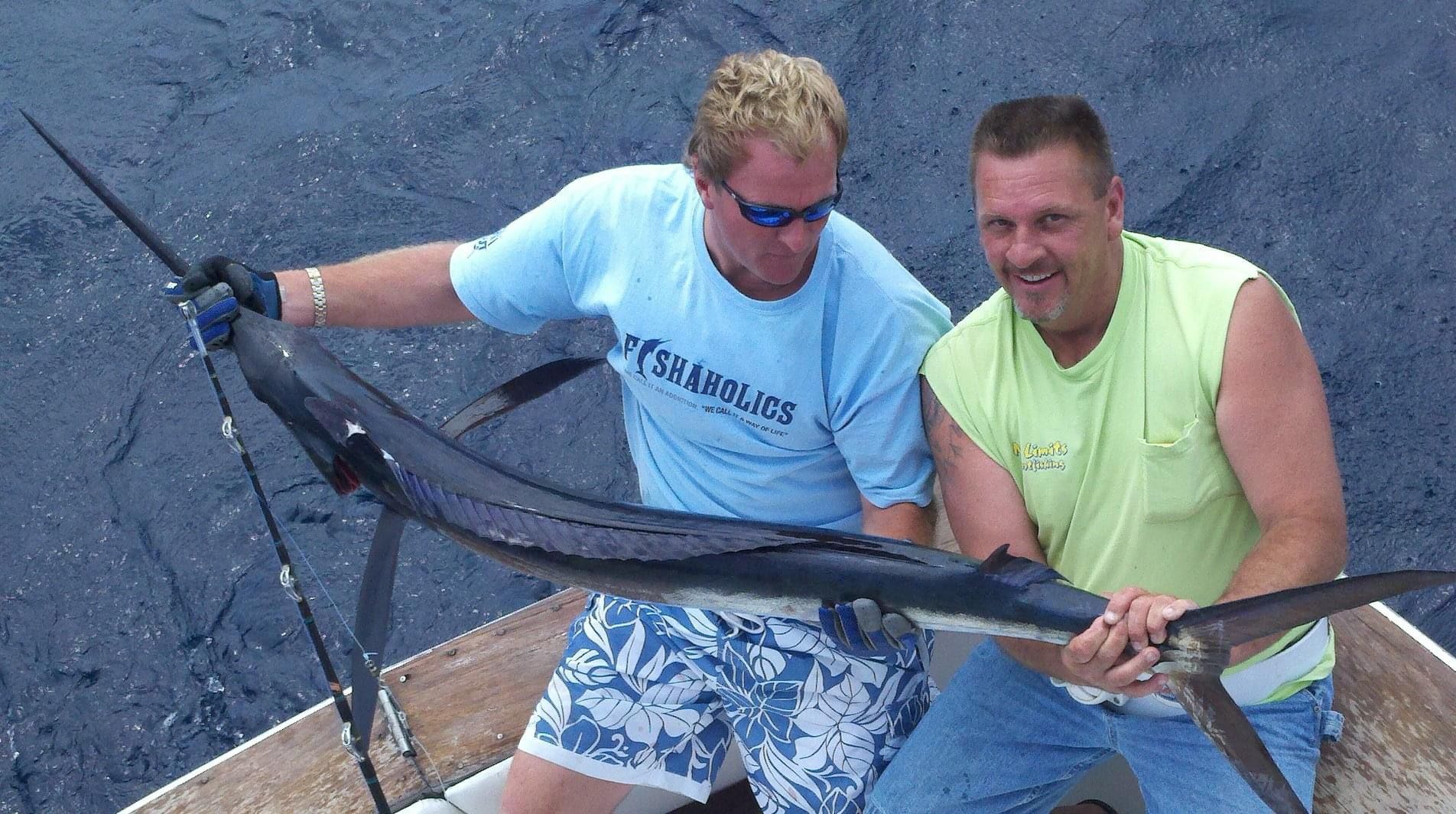 Two men are holding a large fish and one of them is wearing a shirt that says triathlon