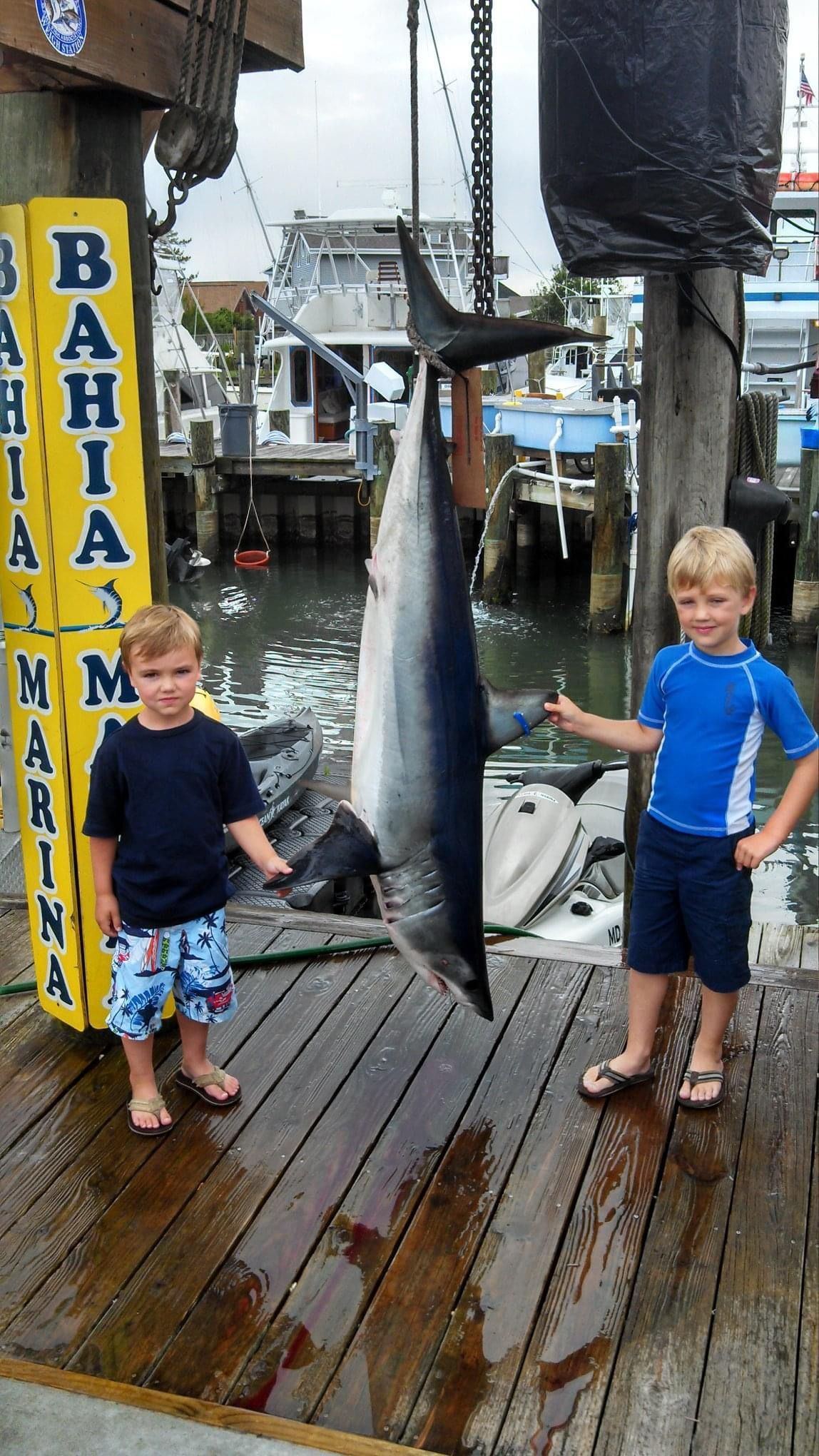 Two young boys holding a large fish in front of a bahia marina sign