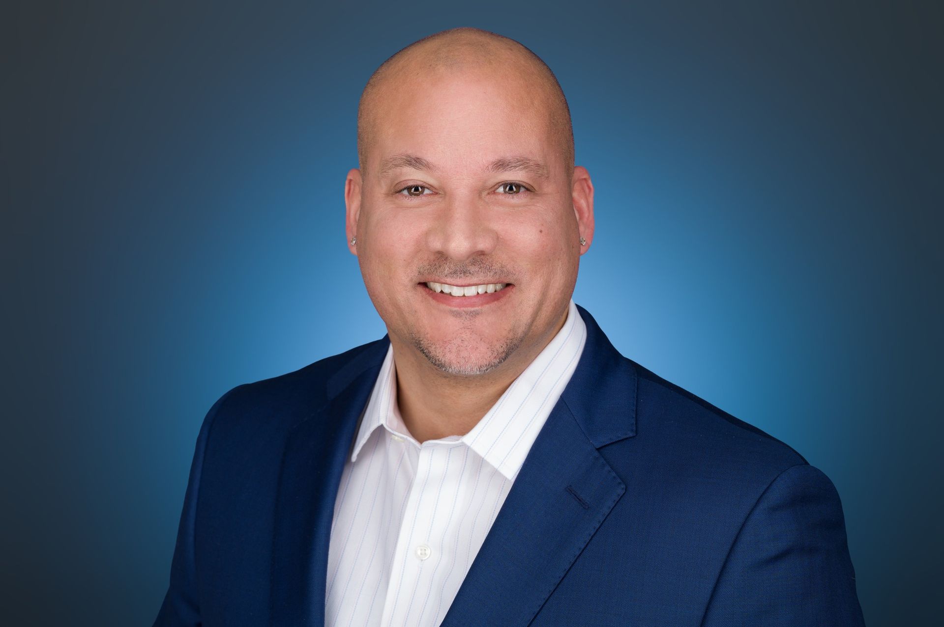 A smiling person in a blue blazer and white collared shirt against a blue gradient background.