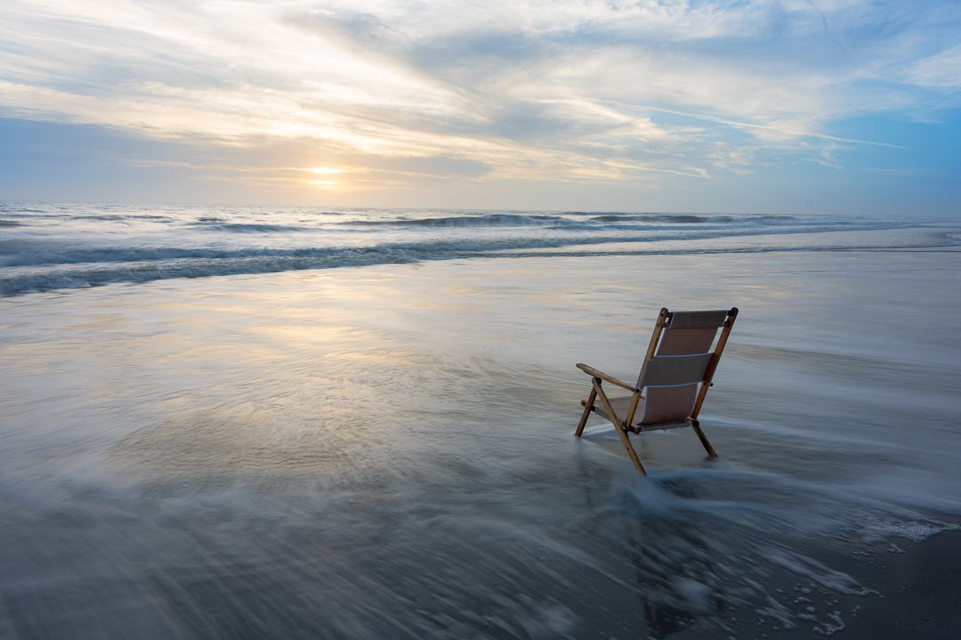 a chair is sitting in the water on a beach at sunrise. Talking Excitingly, Brad Burgess Photograhy