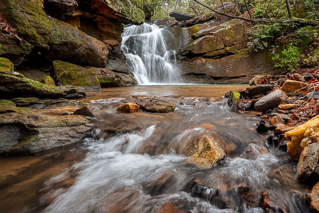 a small waterfall is surrounded by rocks and trees in the woods . Secret Cove Falls, Talking Excitingly, Brad Burgess Photography