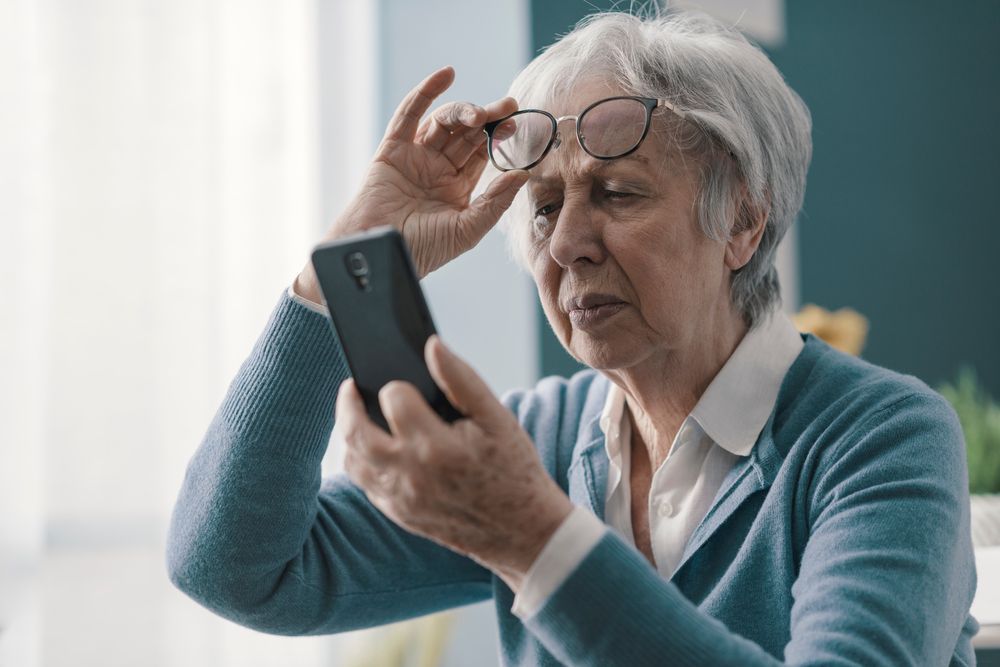 Elderly Woman Holding Up Her Glasses Looking at a Phone — Michael Chu Optometrist in Cairns North, QLD