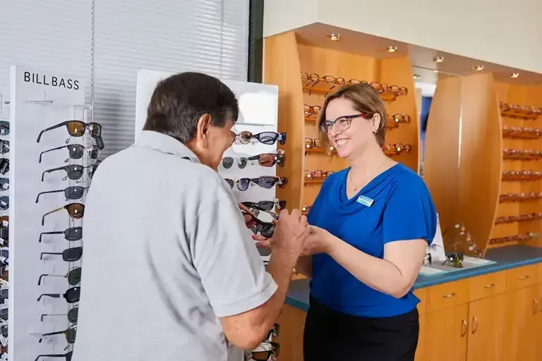 A Woman Assists a Man in Trying on Sunglasses at an Optical Store — Michael Chu Optometrist in Cairns North, QLD