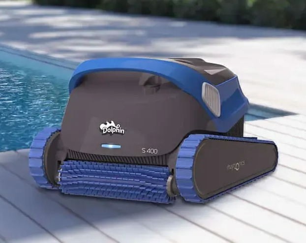 A Dolphin S400 robotic pool cleaner, gray and blue, on a pool deck next to a pool.