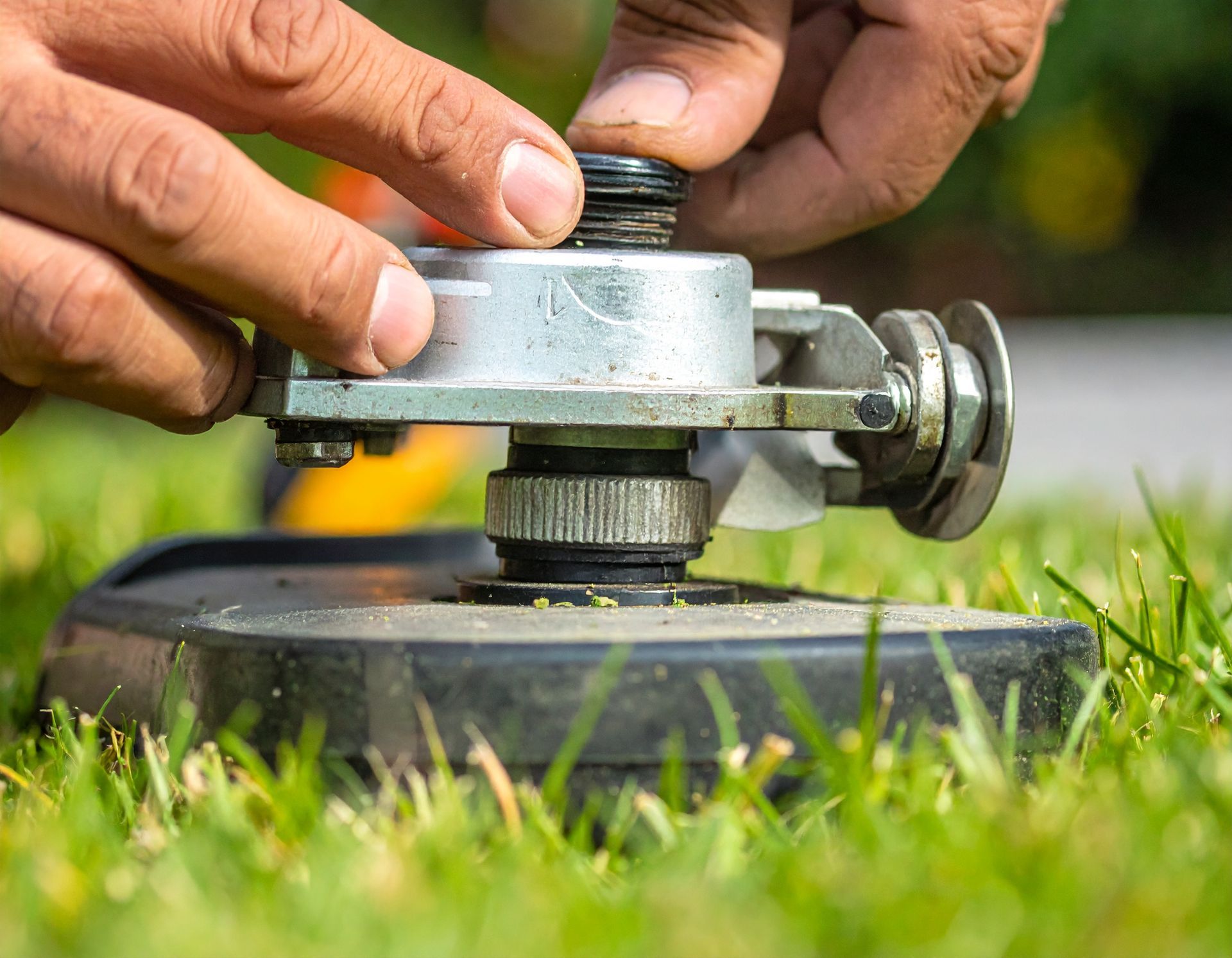 Hands adjusting a lawn mower blade with grass and wheel in the foreground