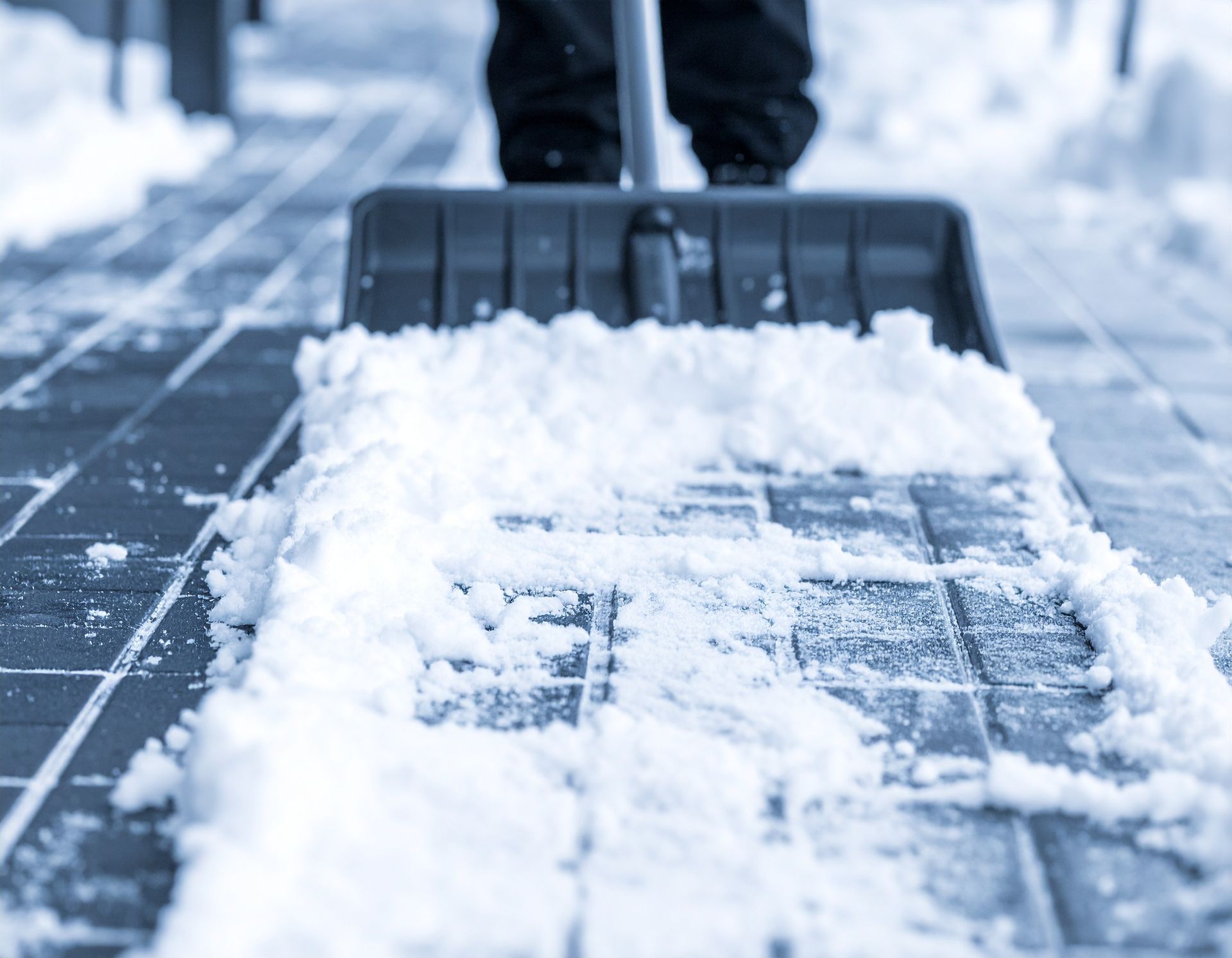 Person shoveling snow from a sidewalk with a black snow shovel