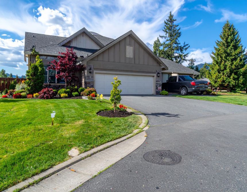 House with a gray garage, lush green lawn, driveway, and a black pickup truck. Blue sky.