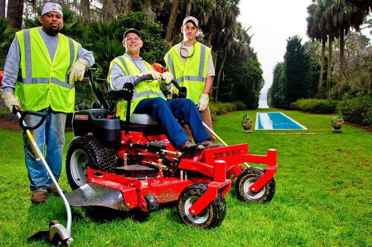 Three men are standing next to a red lawn mower