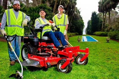 Three men are standing next to a red lawn mower