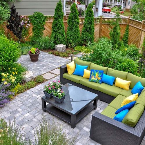 A patio with a couch , table , and umbrella in a garden.