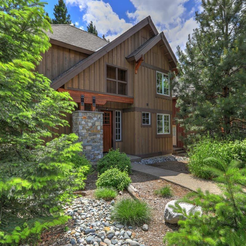A large wooden house is surrounded by trees and rocks.