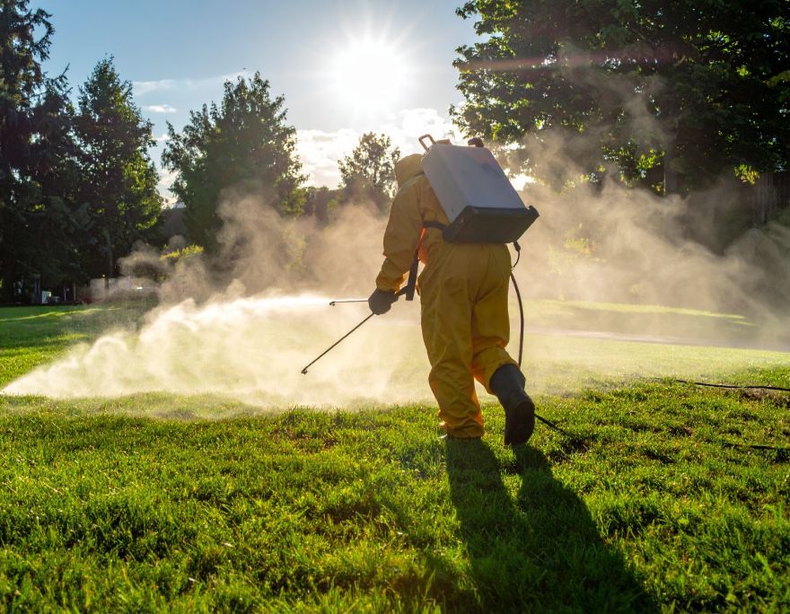 Person in yellow protective suit spraying chemicals on grass outdoors.