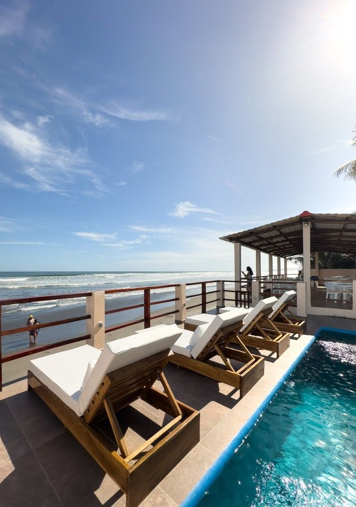 Piscina frente al mar con camastros, vista al mar, cielo azul.