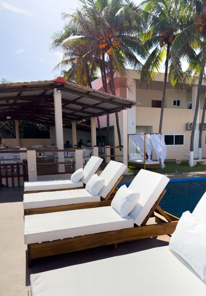 Tumbonas junto a una piscina en un resort con palmeras y un bar a la sombra.