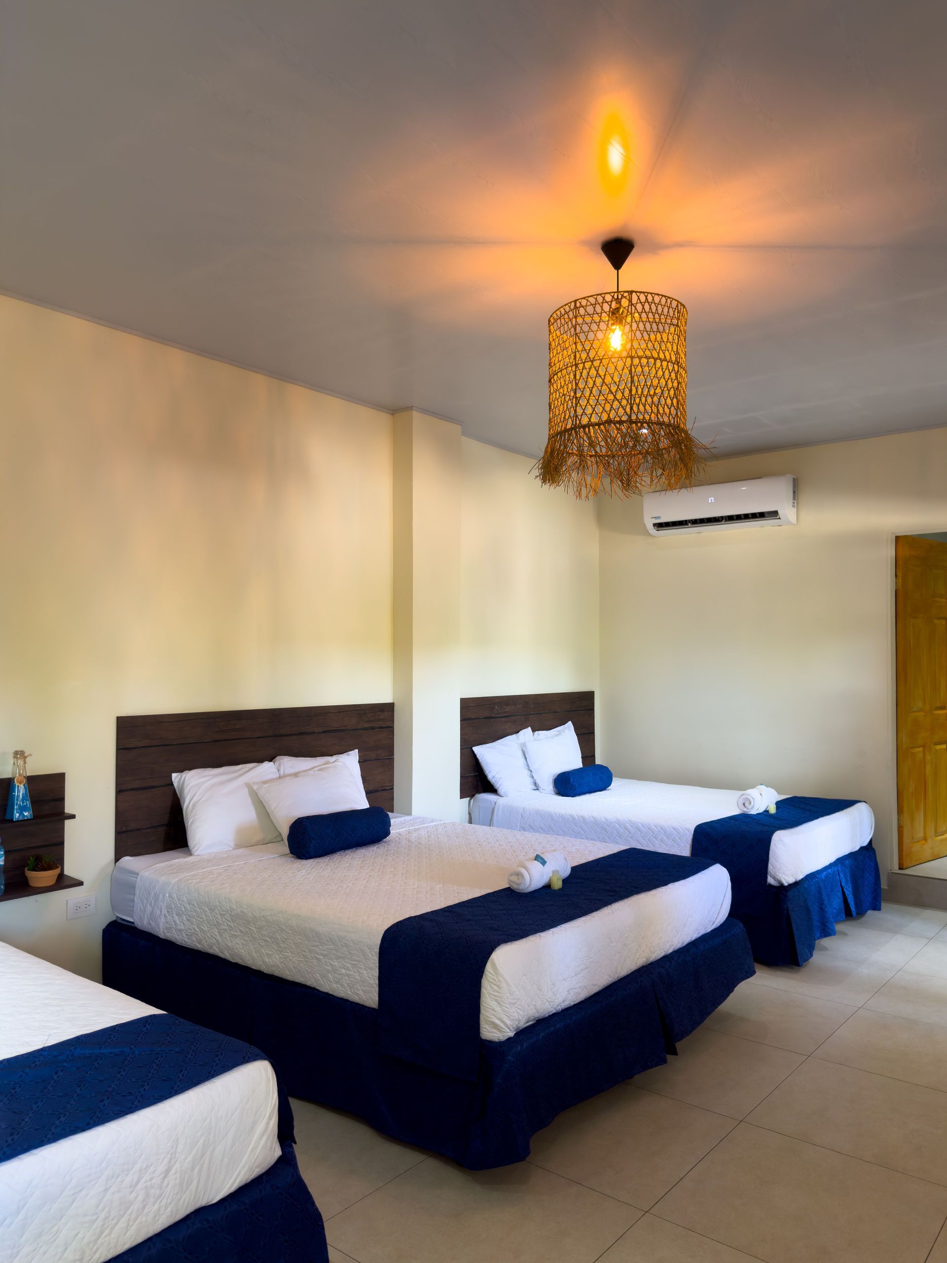 Una habitación de hotel bien iluminada con tres camas, sábanas blancas y detalles azules.