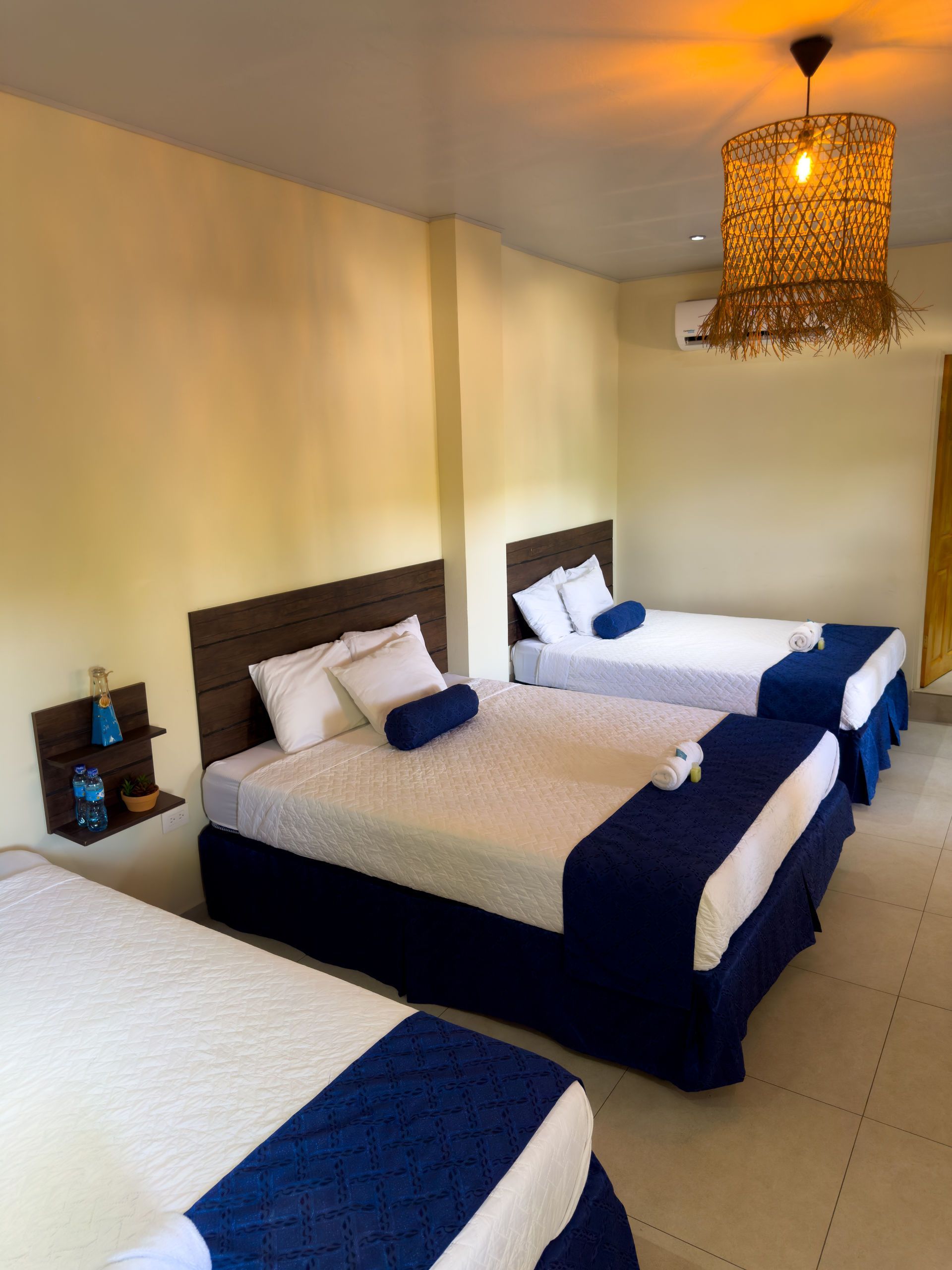 Tres camas en una habitación con detalles azules, cabeceros de madera y una lámpara colgante decorativa.