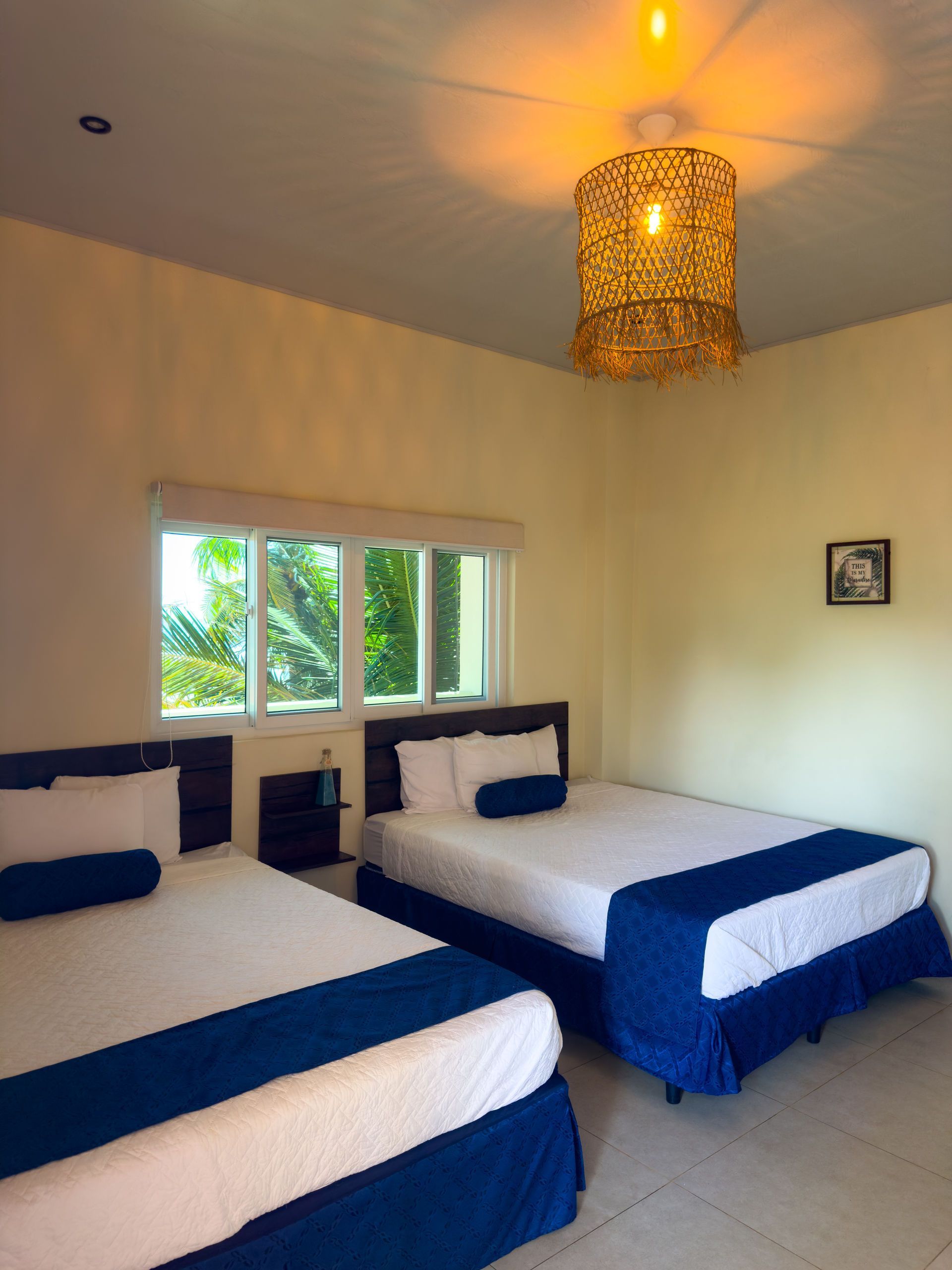 Dos camas en una habitación con detalles azules, una ventana y una lámpara colgante ornamentada.