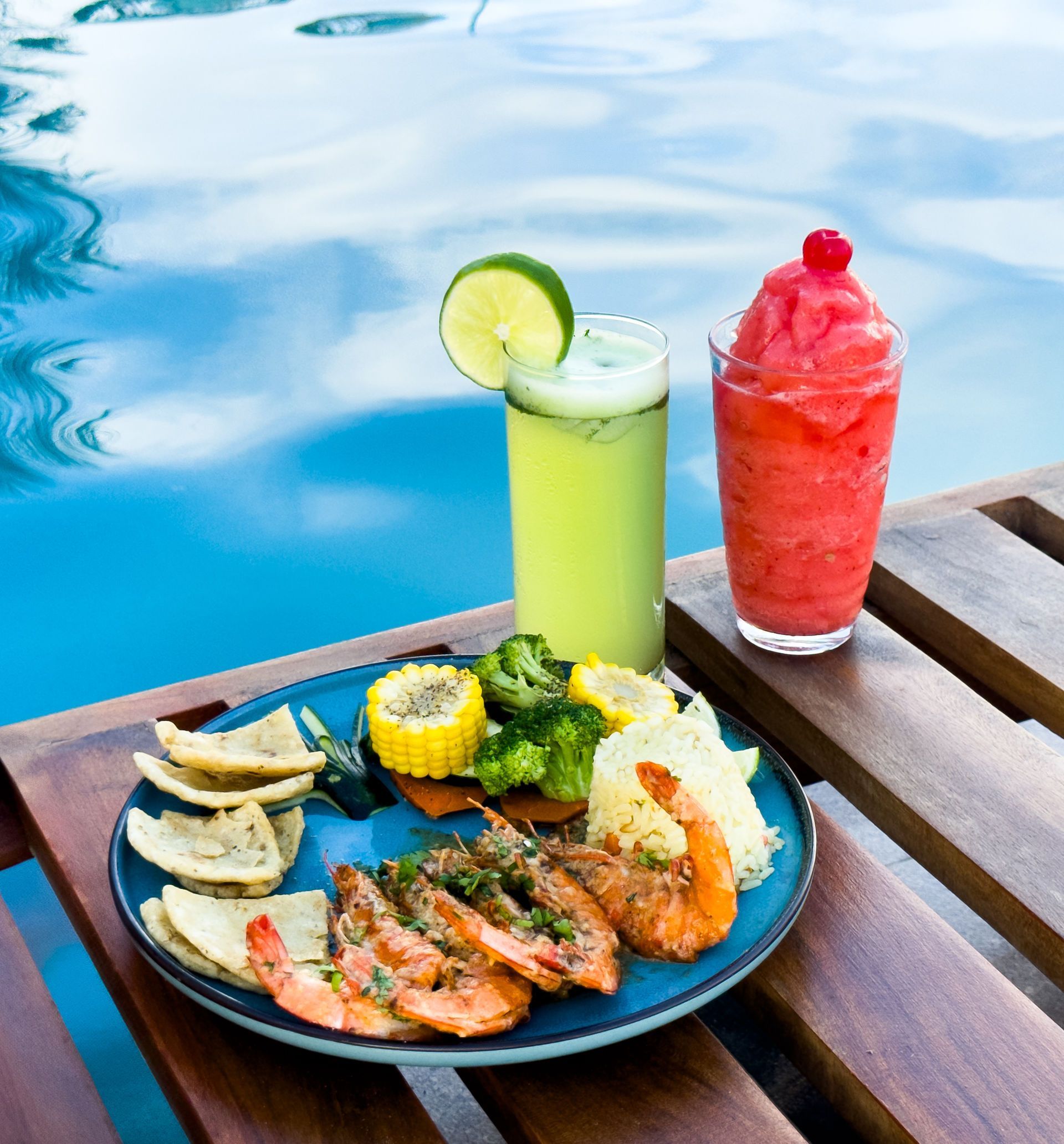 Plato de camarones a la parrilla, guarniciones y bebidas junto a una piscina.