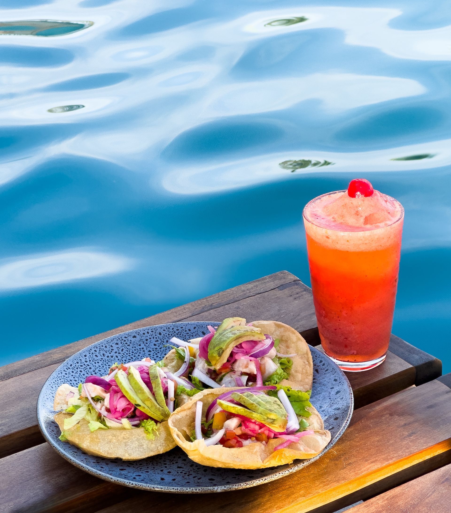 Tacos en un plato azul con una bebida en capas, con un fondo de agua azul.