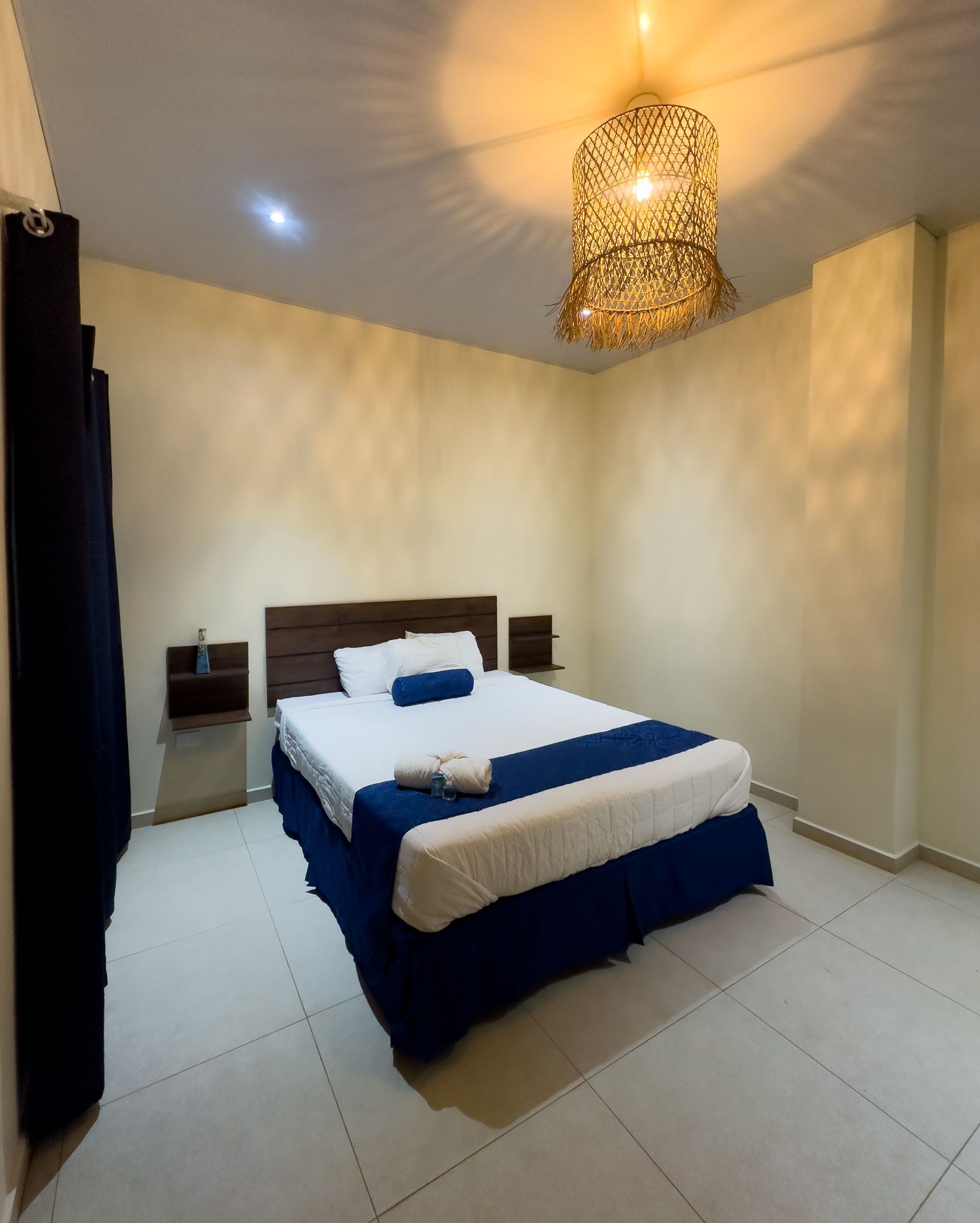 Dormitorio con una cama cubierta con ropa de cama blanca y azul, un cabecero de madera y una lámpara decorativa.