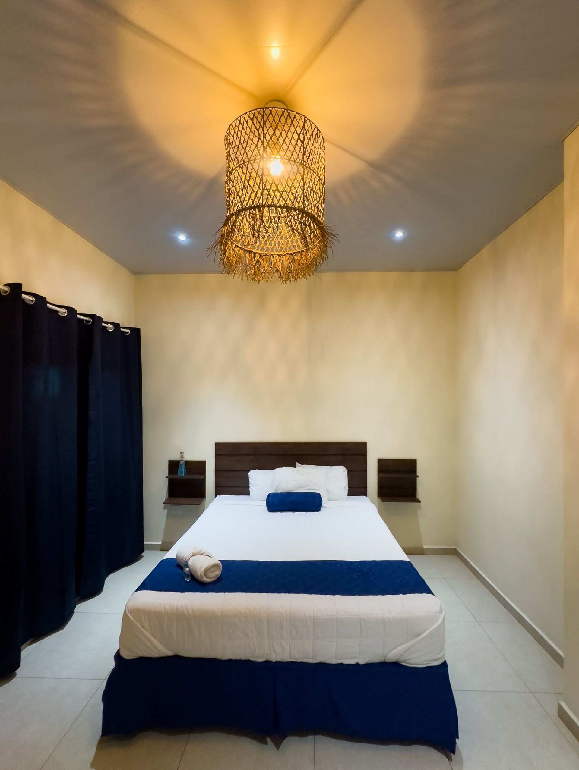 Dormitorio con una cama, cortinas azul oscuro y una lámpara de araña decorativa.