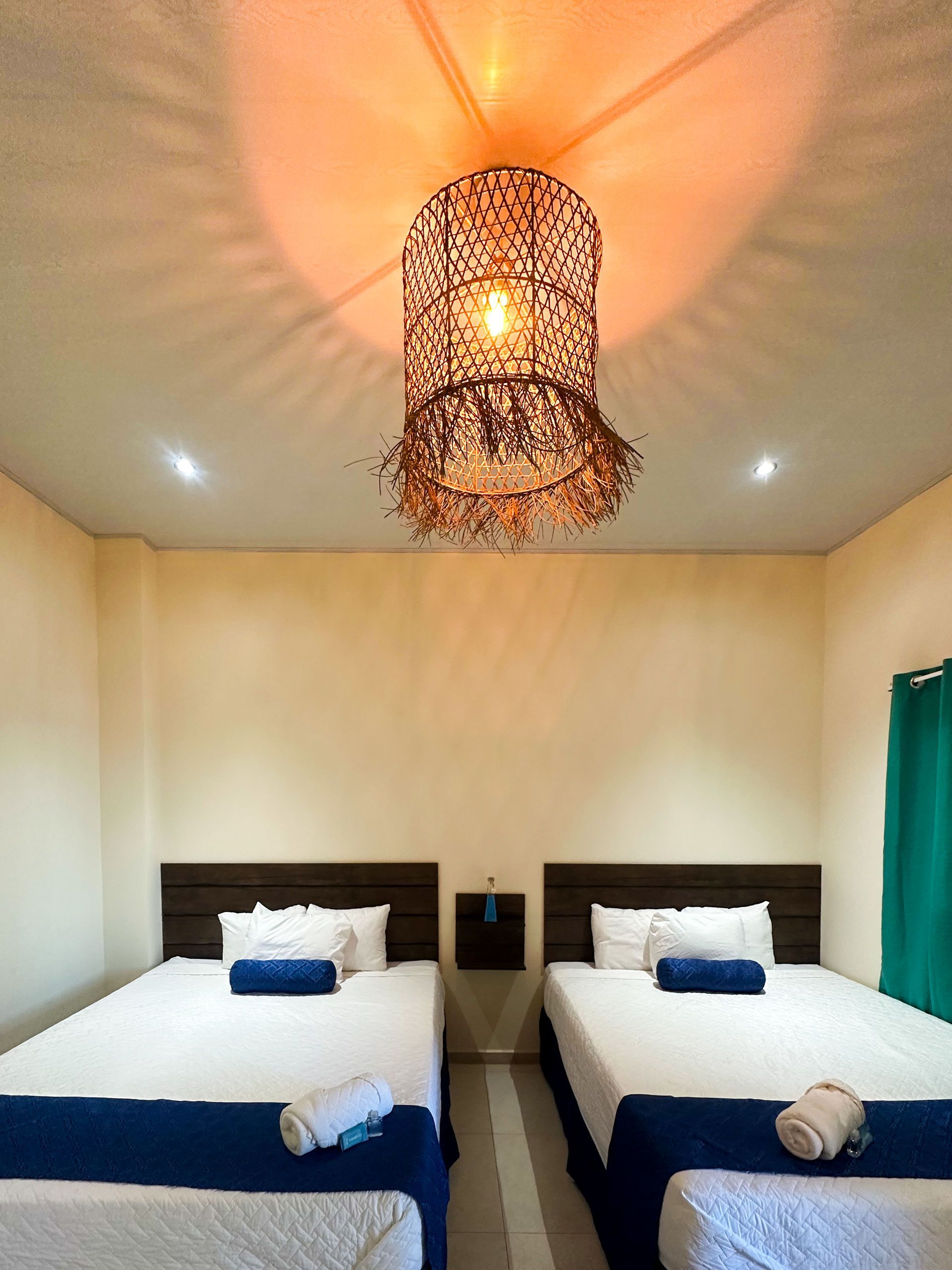 Dos camas en una habitación con cabeceros de madera, sábanas blancas y una lámpara colgante decorativa.