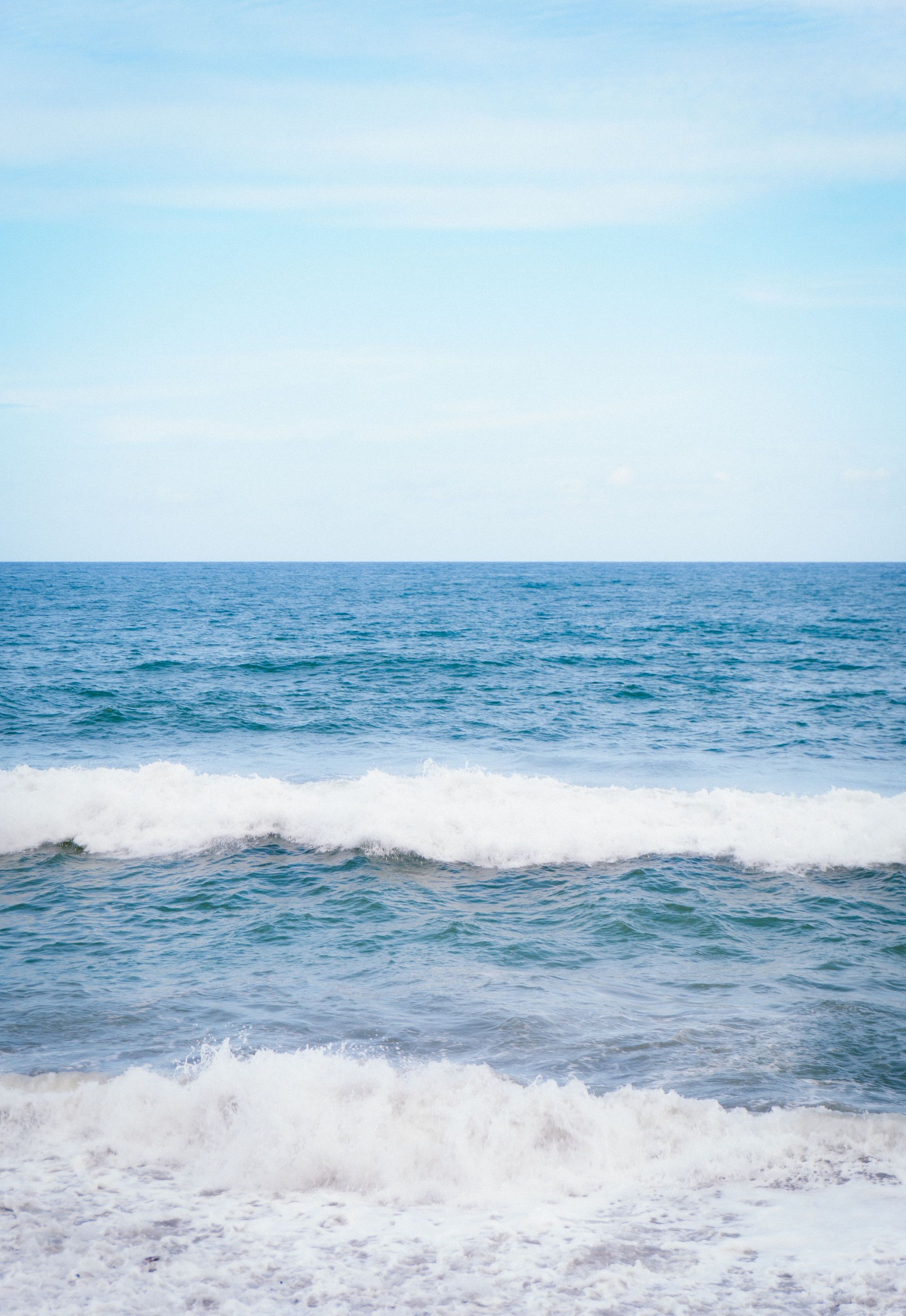 Olas del océano rodando hacia la orilla bajo un cielo azul claro.