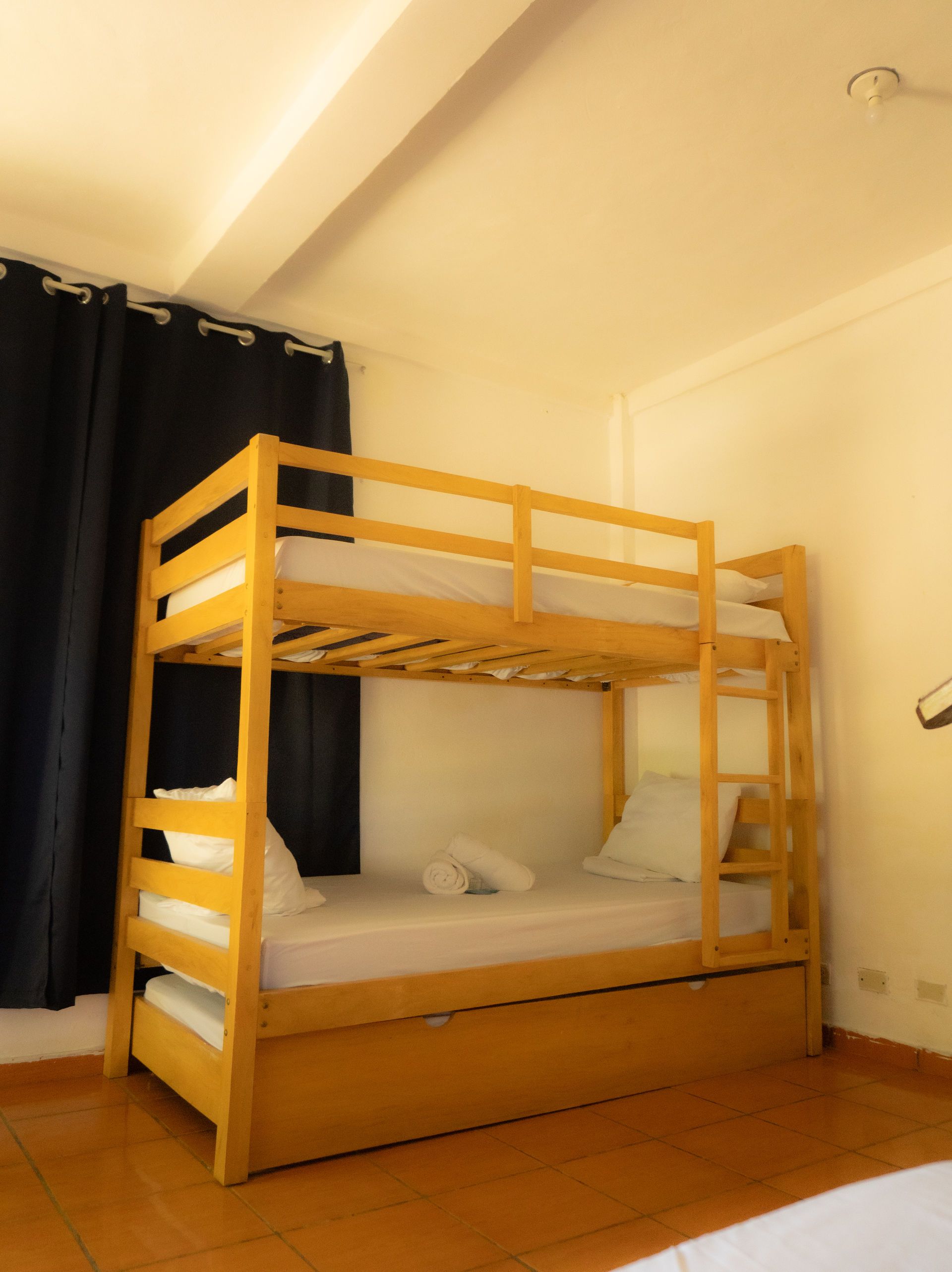 Litera amarilla en una habitación con paredes blancas, cortinas azules y una cama nido.