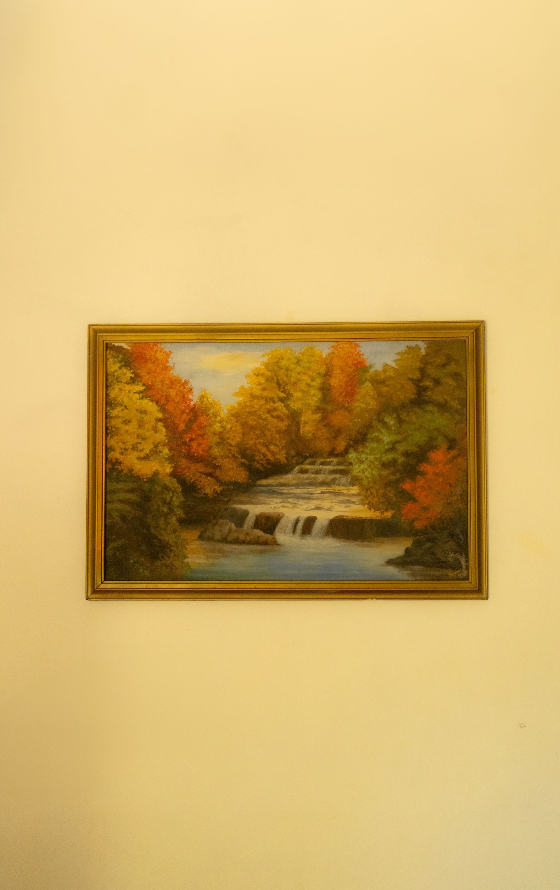 Pintura de una escena de cascada en otoño; marco dorado, árboles coloridos y agua fluyendo.