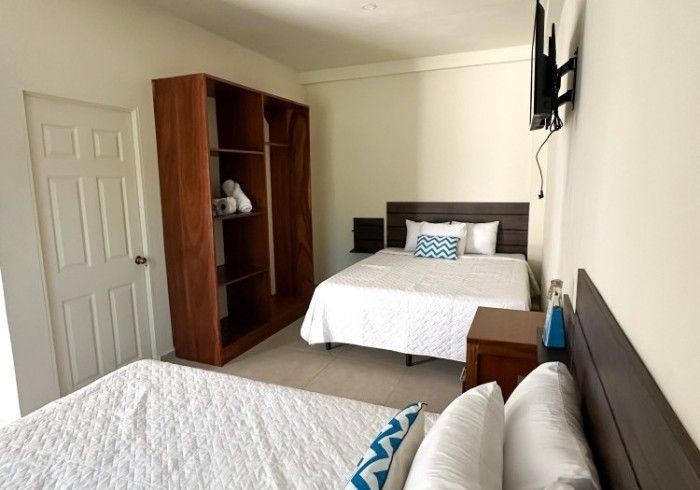 Dormitorio con dos camas, armario y televisión montada en la pared.