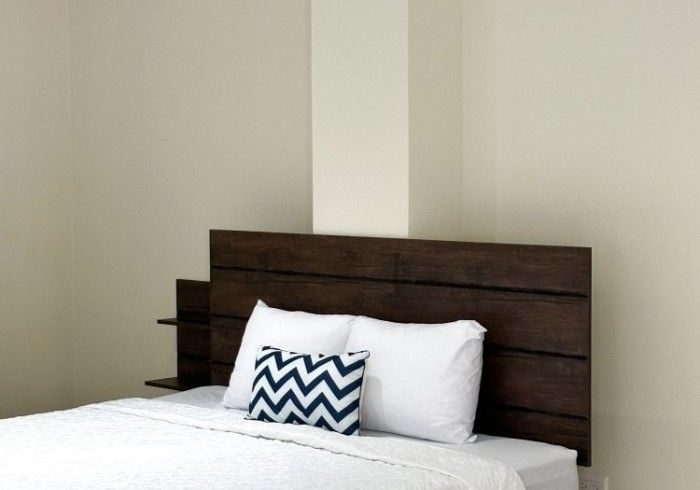 Cama con cabecera de madera oscura, almohadas blancas y una almohada de chevron azul en una habitación de tonos neutros.