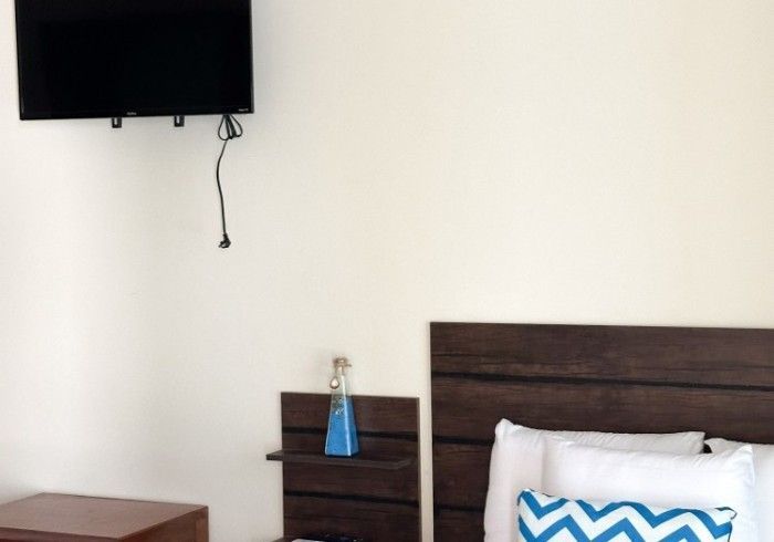 Dormitorio con TV montada, cabecero de madera, botella decorativa azul y mesita de noche.