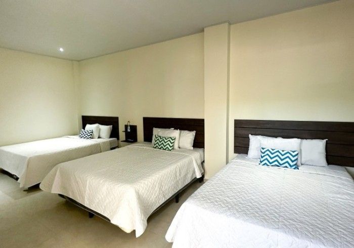 Tres camas en una habitación con ropa de cama blanca, cabeceros de madera oscura y un fondo de pared claro.