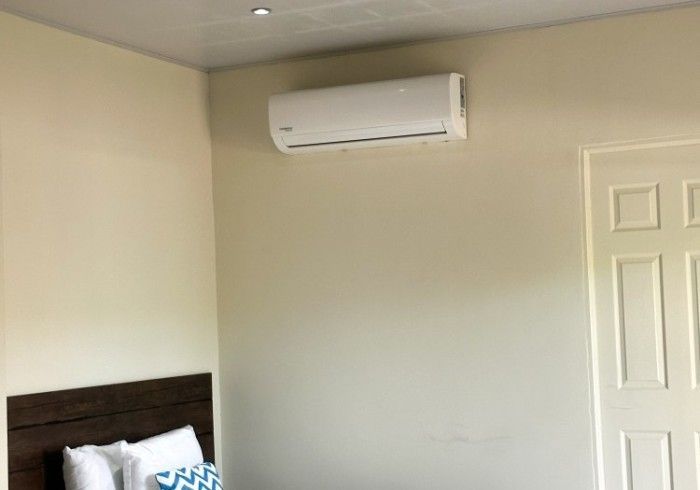 Unidad de aire acondicionado montada en una pared beige en una habitación con cabecero de madera y puerta blanca.