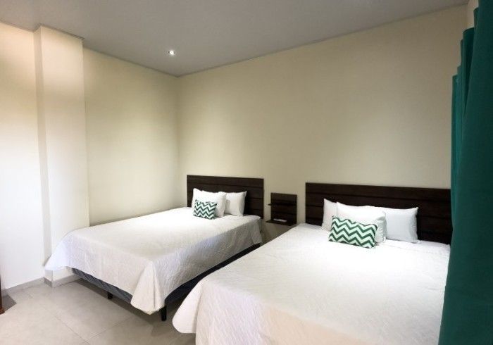 Dos camas con ropa de cama blanca en una habitación beige. Un cojín verde azulado cada una.