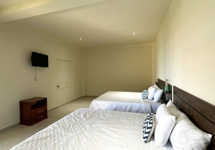 Dormitorio con dos camas queen, ropa de cama blanca, cabeceras de madera oscura, televisor pequeño y mesita de noche.