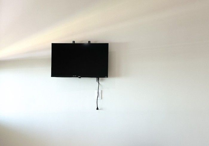 Televisor de pantalla plana montado en una pared blanca con cables colgando debajo.