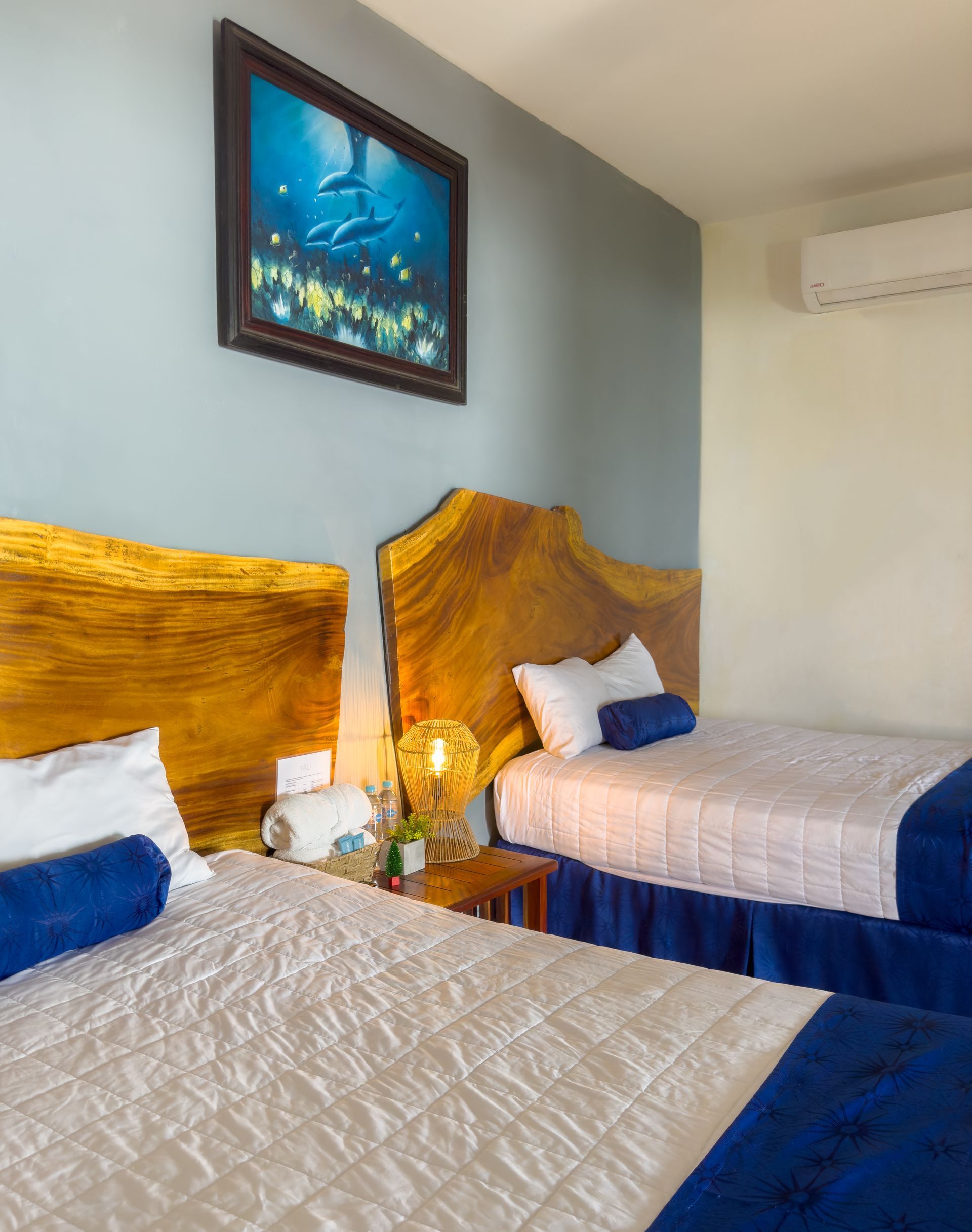 Dos camas individuales con cabeceras de madera, edredones blancos y detalles azules en una habitación con arte de delfines.
