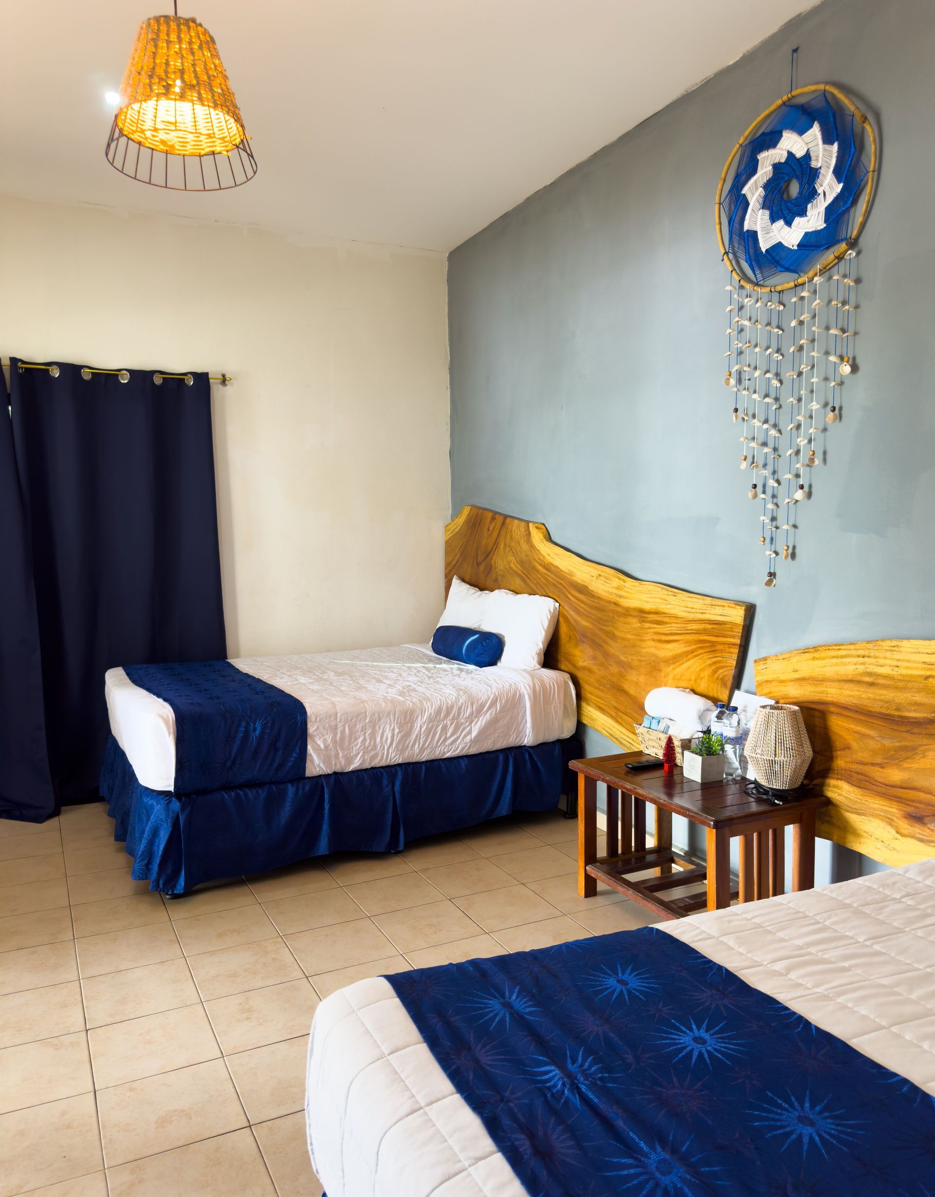 Dos camas individuales en un dormitorio con cabeceros de madera, detalles azules y un atrapasueños en la pared.