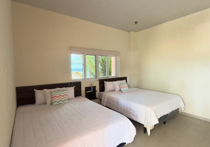 Habitación con dos camas y ventana al mar. Sábanas blancas y paredes claras.