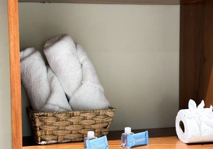 Cesta con toallas blancas dobladas, artículos de tocador y rollos de papel dentro de un armario de madera.