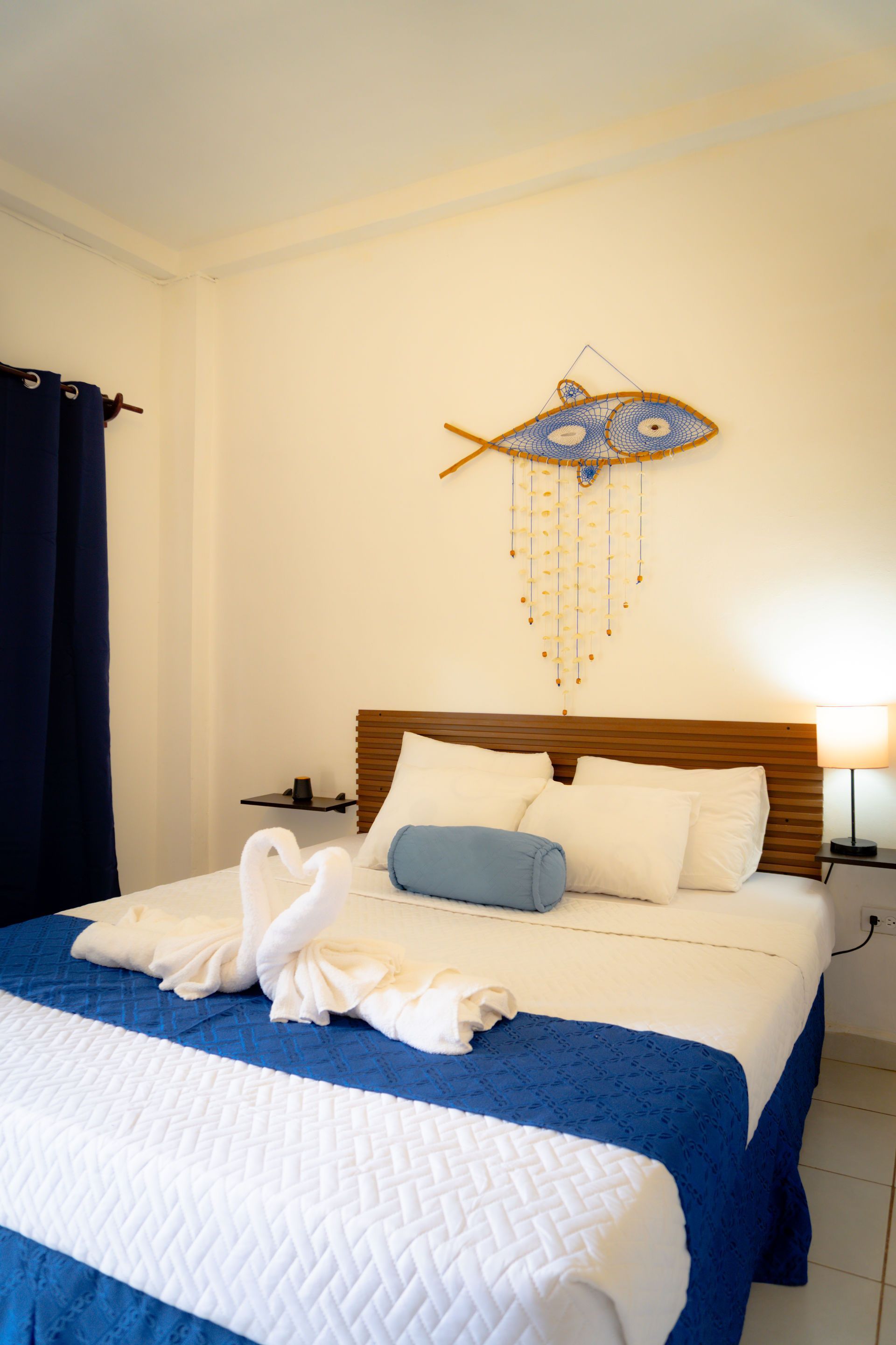 Dos camas individuales en una habitación luminosa; ropa de cama blanca, almohadas coloridas y obras de arte con una ventana.